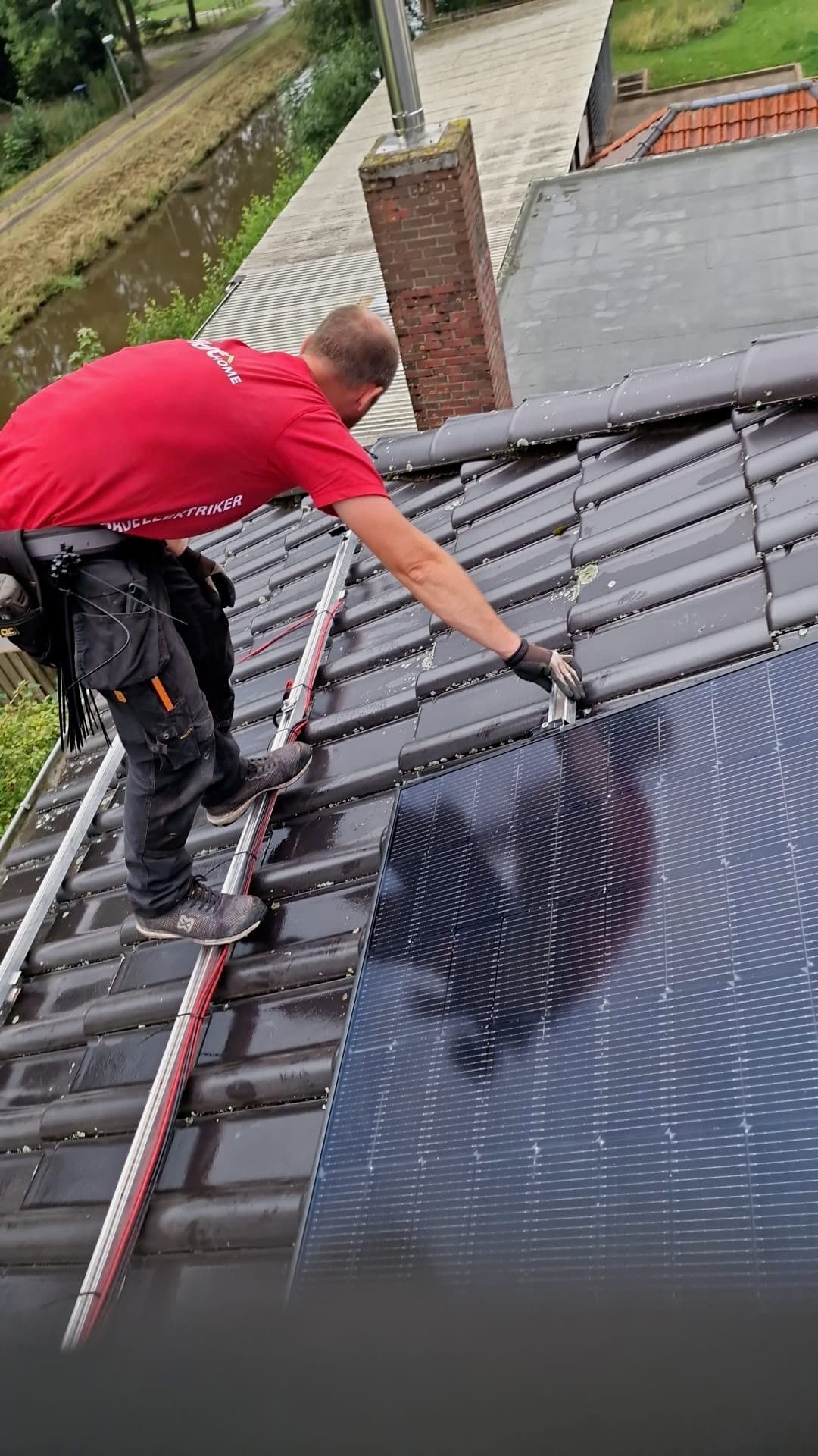 BSH-Monteur im roten Shirt verlegt ein PV-Modul auf dem Dach